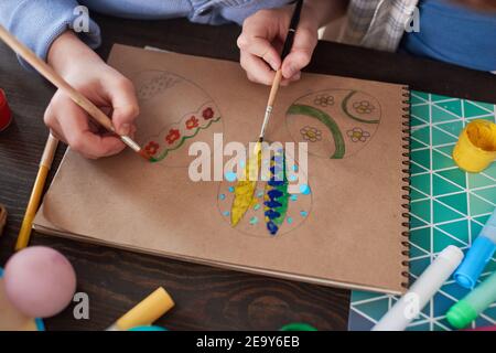 Close-up of children painting Easter eggs on paper with paint brushes at the table during art classes Stock Photo