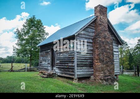 A picturesque setting of an old farm homestead roadside in a farm field surrounded by a rustic wooden fence and trees on a bright sunny day in summert Stock Photo