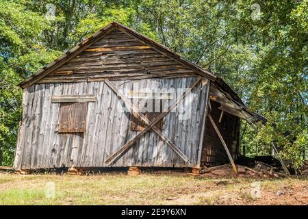 Abandoned old wooden farmhouse collapsing from neglect and time boarded up and falling off the stone foundation on a sunny day in summer Stock Photo