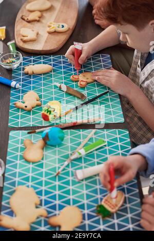 Close-up of kids sitting at the table decorating gingerbread shapes with a food coloring for Easter holiday Stock Photo