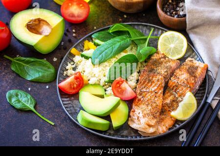 Grilled salmon fillet with couscous, salad fresh vegetables and avocado on dark background. Stock Photo