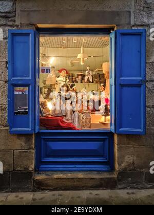 Spain; Dec 2020: Puppets on display made of papier mâché and wood, traditional shop pictured through a blue window on a facade made of stone. Warm lig Stock Photo