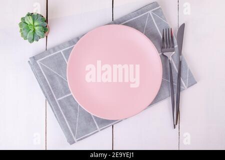 Close up top view of serving empty pink plate, knife and fork on folded linen napkin with geometric pattern. Selective focus. Mockup, copy space, mini Stock Photo