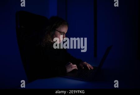 Young woman with headphones typing on her laptop at the night. Blue ambient lights. Stock Photo