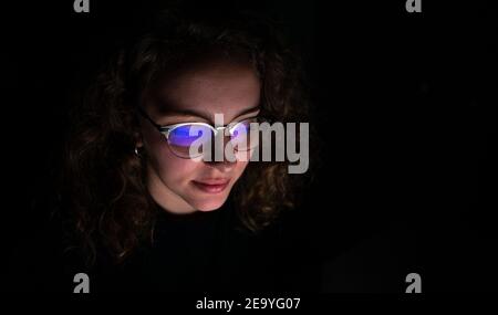 Happy woman working at night with her computer. The room is dark and the screen is reflected in her glasses. Stock Photo
