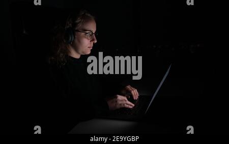 Business woman overworking with computer at night. She has the wireless headphones on. Stock Photo