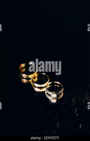 three gold rings lie next to each other on a mirror background, wedding accessories on a black background Stock Photo