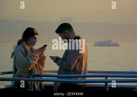 Young couple using smartphones and weaking masks on Izmir ferry Stock Photo