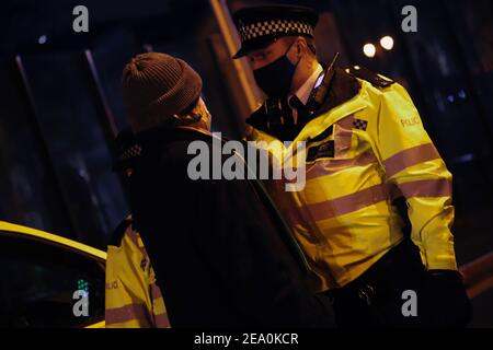 London, UK. 6th February, 2021. Candlelit vigil in remembrence of the lost trees at Euston Square, London as part of the Stop HS2 protest February 6th 2021. A police officer challenges a protestor Credit: Denise Laura Baker/Alamy Live News Stock Photo