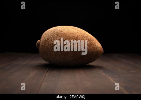 still life image of one mexican red mamey close up on rustic wooden surface and black background Stock Photo