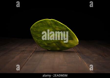 still life image of one organic nopal pad from Mexico. Raw and clean no spikes ready to cook. Close up on rustic wooden surface and black background Stock Photo