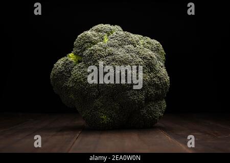 still life image of raw broccoli head crown close up on rustic wooden surface and black background Stock Photo