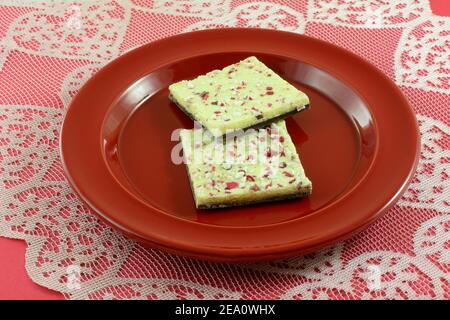 White chocolate peppermint bark on top of dark chococlate candy on red plate on heart lace tablecloth runner Stock Photo