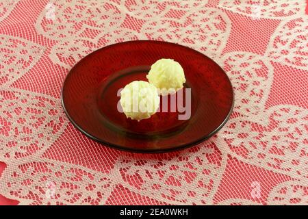 White chocolate truffle candy on red plate on heart lace on red table Stock Photo