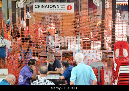 Chinatown, Singapore 3 Feb 21: Middle-aged men playing Chinese Chess, while others watch at a safe distance behind plastic fencing Stock Photo
