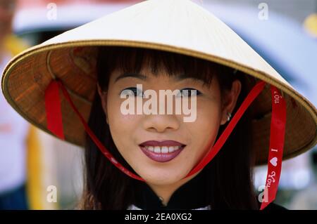 Vietnam, Ho Chi Minh City aka Saigon, Portrait of pretty smiling young Vietnamese Woman Wearing traditional Conical Hat Stock Photo