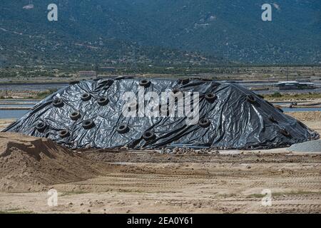 Storage warehouse of mineral construction materials in outdoors.  Pile of rubble is covered with a protective film from the weather. Stock Photo