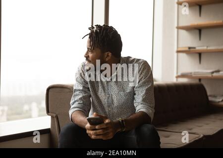 Happy african guy look at window with smartphone in hands Stock Photo