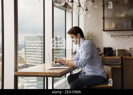 Concentrated young man modern designed studio flat owner using laptop Stock Photo