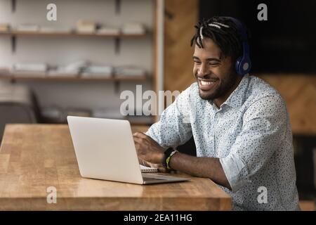 Laughing millennial afro guy in earphones relax by pc screen Stock Photo