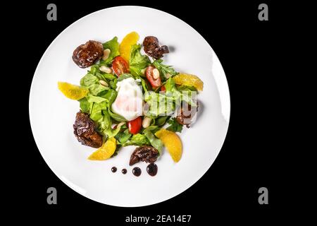 A dish of meat,lettuce, oranges, nuts and chicken eggs, drizzled with sauce in bowl on black background Stock Photo