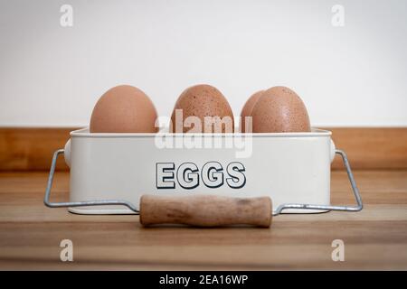 Classic retro cream coloured gloss egg tin tray holding six large free range fresh eggs in container with text on front and wooden hand to carry Stock Photo