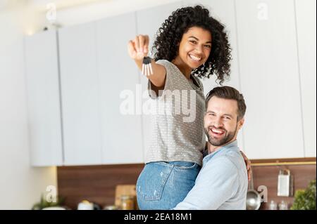 Dreams came true. Excited multiracial couple buying a property, got a mortgage apartment. A guy is carrying his beautiful girlfriend on the arms with Stock Photo
