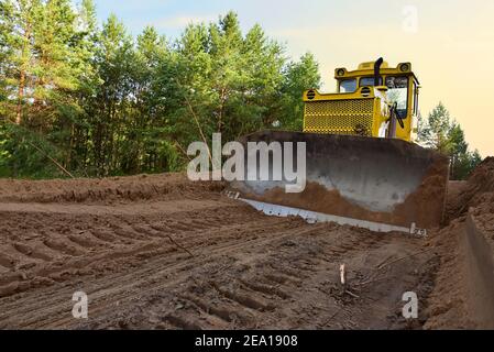 Dozer during clearing forest for construction new road . Yellow Bulldozer at forestry work Earth-moving equipment at road work, land clearing, grading Stock Photo