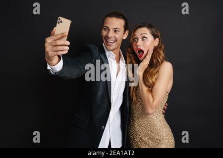 Couple in smart wear celebrating holiday party taking a selfie isolated on black background Stock Photo