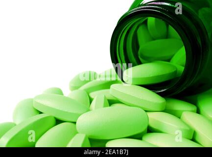 Oval shaped lime green tablets poured from dark green glass bottle on white background Stock Photo
