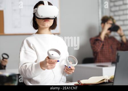 team of four creative engineers working with virtual reality, young woman testing VR glasses or goggles sitting in the office room Stock Photo