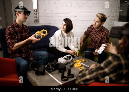 team of four creative engineers working with virtual reality, young woman testing VR glasses or goggles sitting in the office room Stock Photo