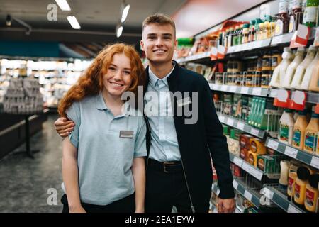 Portrait of two young workers standing together in supermarket. Male and female employees smiling at camera in grocery store Stock Photo
