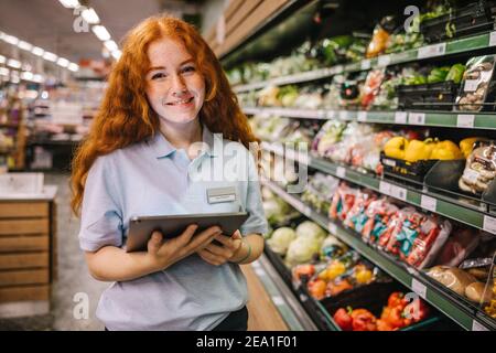 Closeup of a young worker with digital tablet in grocery store. Happy trainee working in supermarket. Stock Photo