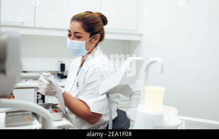 Dentist doing a dental treatment in teeth of a patient using tools. Female dental doctor wearing face mask working in her clinic. Stock Photo