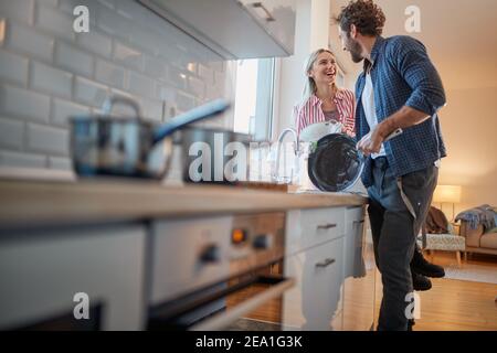 A young couple doing housework with satisfaction in a cheerful atmosphere. Kitchen, housework, home, relationship Stock Photo