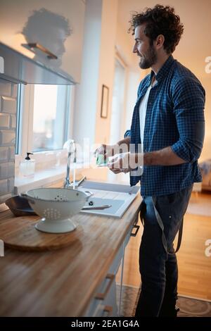 Young man enjoying doing housework in a relaxed atmosphere in the kitchen. Kitchen, housework, quarantin, home Stock Photo