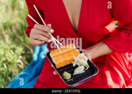 Close-up sushi set. Attractive girl holds sushi with chopsticks in hands. Courier delivered sushi set for pretty woman. Black box with sushi, wasabi, Stock Photo