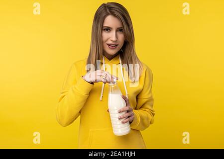 Photo of attractive lady holds bootle of milk, feels nice about dairy products. Wears casual yellow hoody, isolated yellow color background Stock Photo