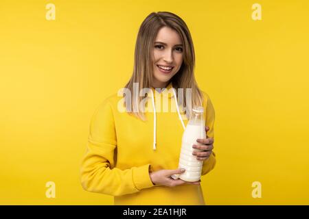 Photo of attractive lady holds bootle of milk, feels nice about dairy products. Wears casual yellow hoody, isolated yellow color background Stock Photo