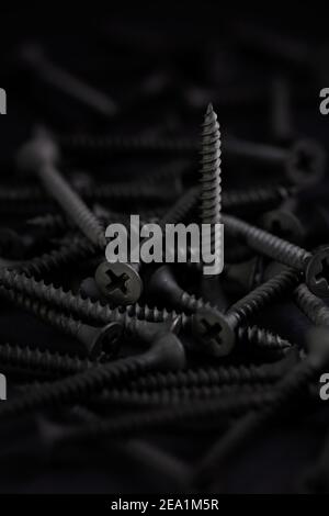 Pile of screws with flat head and phillips drive, in a dark key Stock Photo