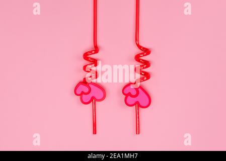 Two red plastic drinking straws with hearts on a pink background. Stock Photo