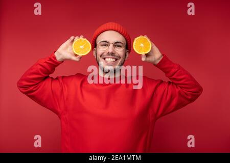 Photo of happy man with beard in red clothing. Holds orange and smiles, isolated over red background Stock Photo