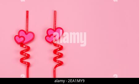 Two red plastic drinking straws with hearts on a pink background. Stock Photo