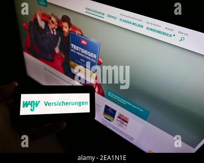 Person holding cellphone with business logo of German insurance company WGV Versicherungen on screen in front of website. Focus on cellphone display. Stock Photo