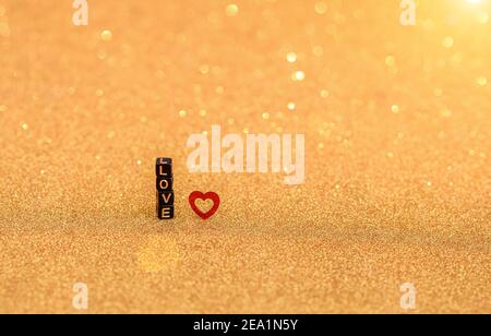 The inscription love made from wooden letters and little heart on a golden iridescent background. Valentine's Day and love concept.  Stock Photo