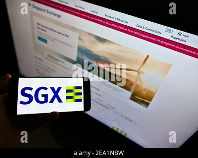 Person holding smartphone with business logo of stock exchange Singapore Exchange (SGX) on screen in front of website. Focus on phone display. Stock Photo