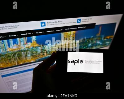 Person holding cellphone with logo of South African Petroleum Industry Association (SAPIA) on screen in front of web page. Focus on phone display. Stock Photo