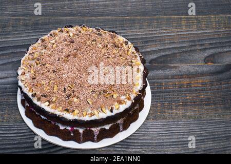 Chocolate cake decorated with grated chocolate with walnuts with fruit filling on a gray wooden vintage background. Background. The concept of making Stock Photo