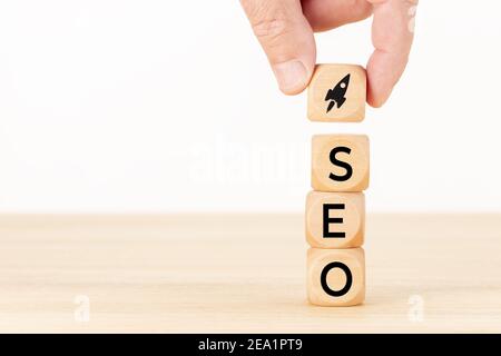 SEO or search engine optimization concept. Human hand holding a wooden block with rocket icon and SEO word. White background Copy space Stock Photo